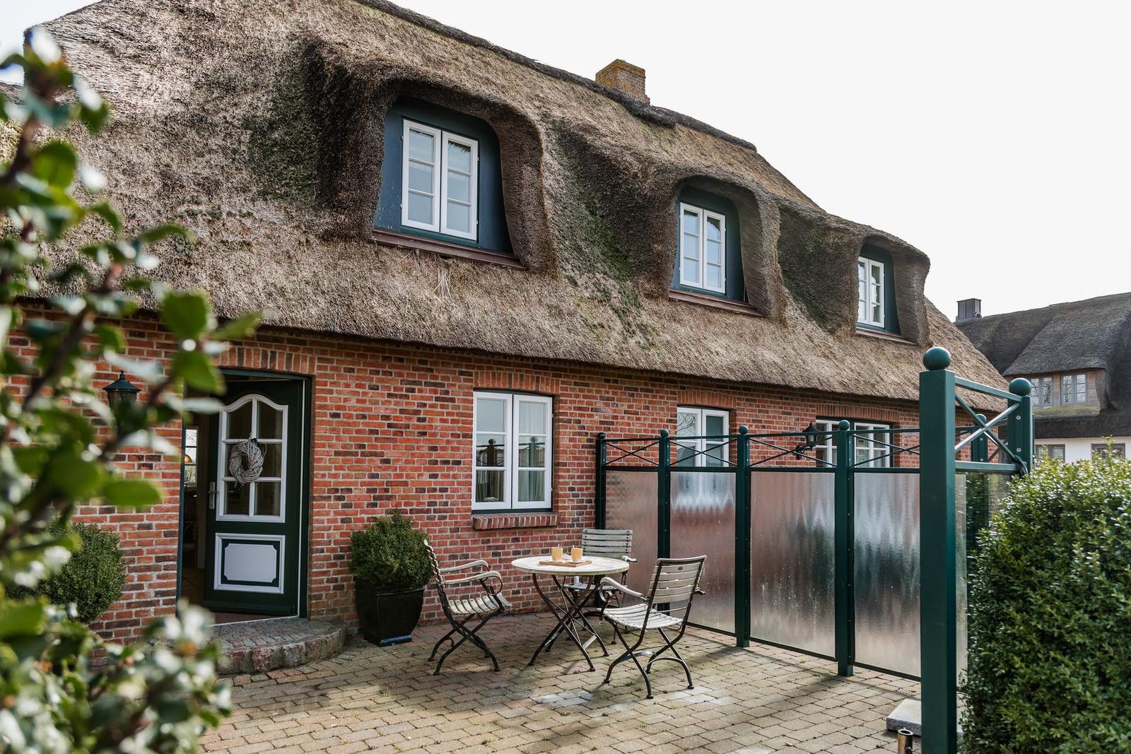 Haus mit Strohdach, Terrasse mit Tisch und Stühlen, Eingangstür und Fenster
