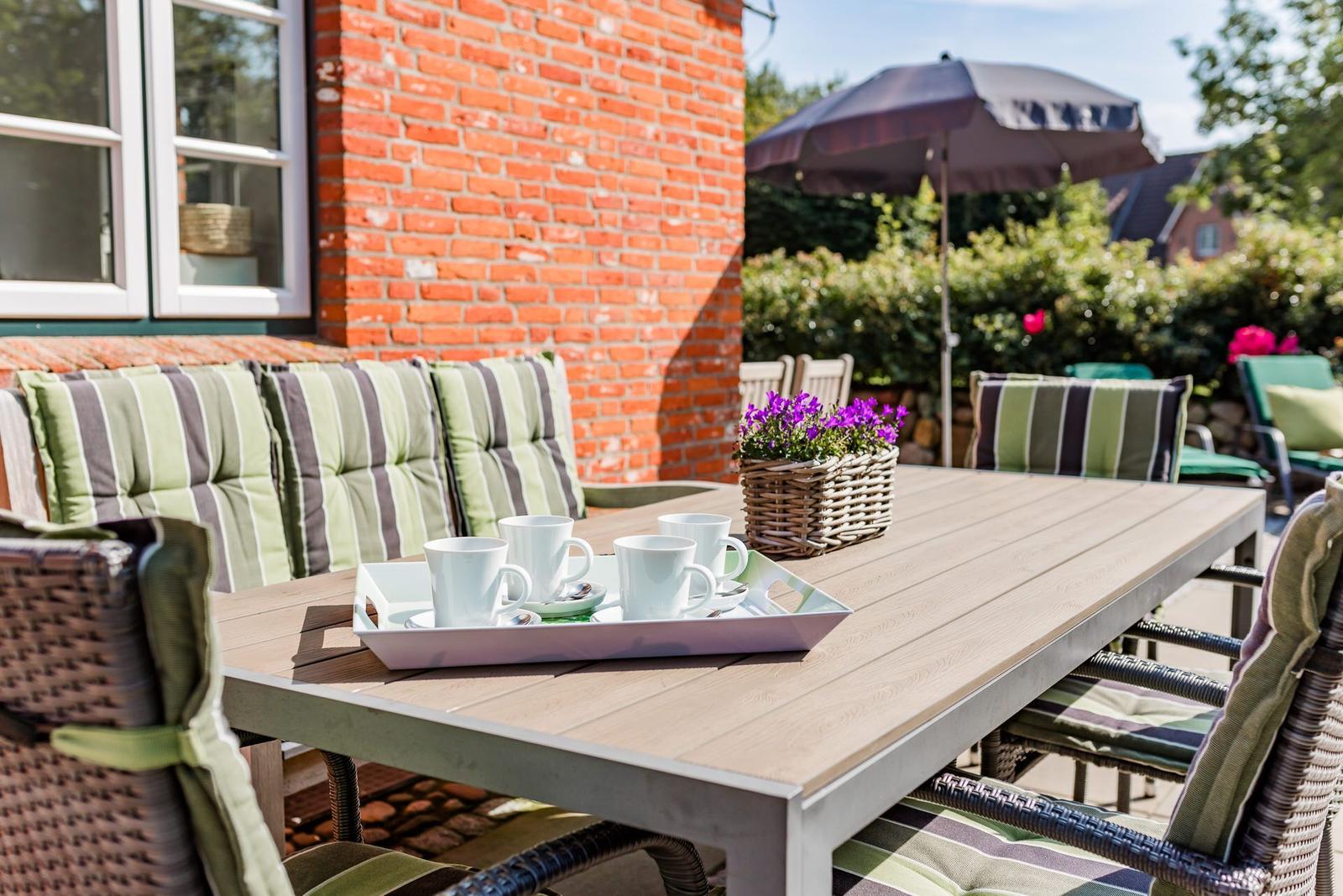 Terrasse mit Tisch, Stühlen und Kaffeetasse. Hintergrund: rote Ziegelwand und Garten.