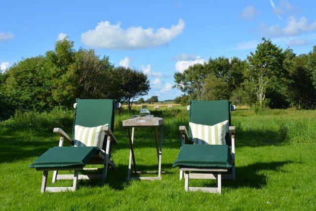 Zwei grüne Liegestühle mit Streifenkissen und Tisch im Gras vor Bäumen.