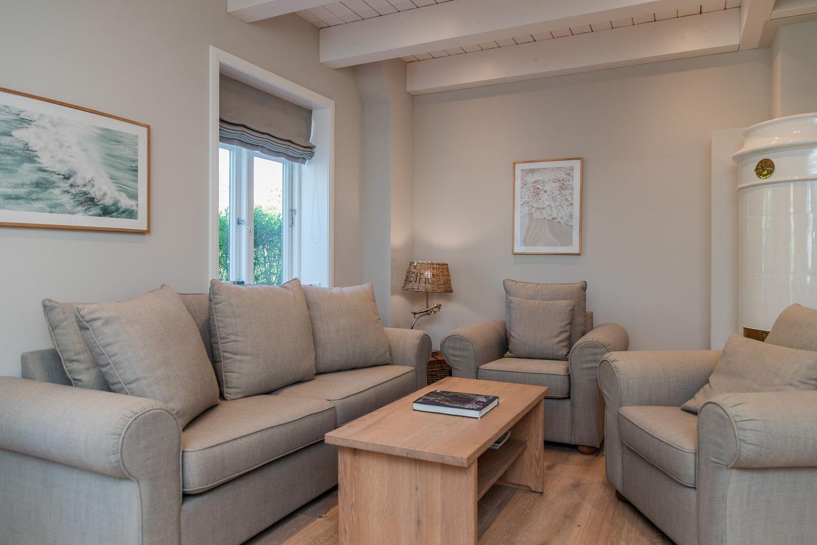 Wohnzimmer mit Sofa, zwei Sesseln, Holztisch und Fenster.