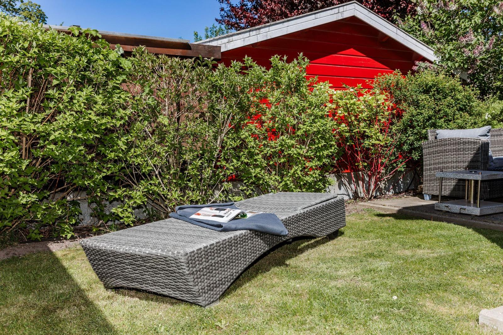 Garten mit Liegestuhl, Grasfläche und rotem Holzhaus im Hintergrund.
