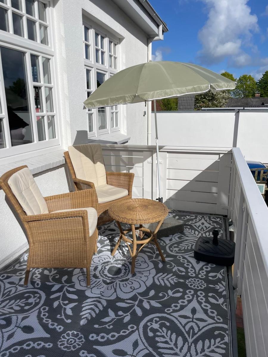 Terrasse mit zwei Stühlen, Tisch und Sonnenschirm auf gemustertem Teppich.