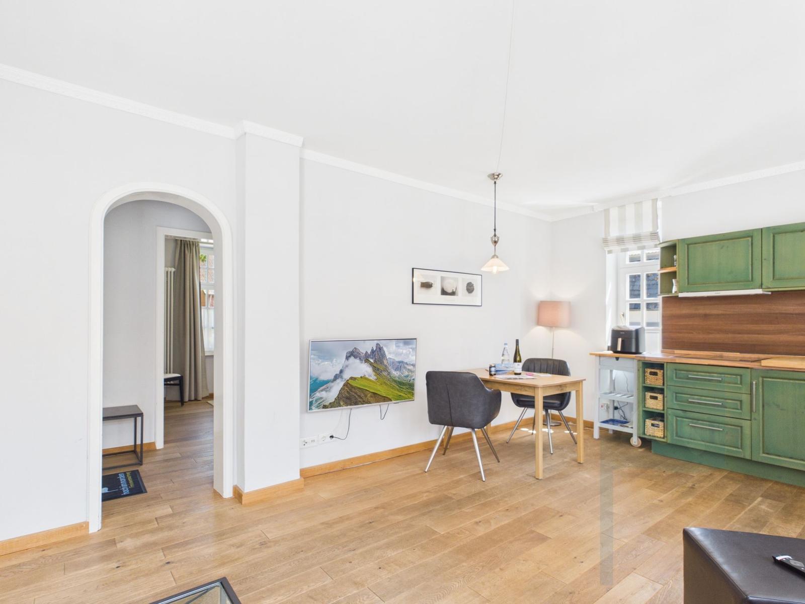 Wohnküche mit grünen Schränken, Esstisch und Wandbild. Durchgang zu Schlafzimmer.