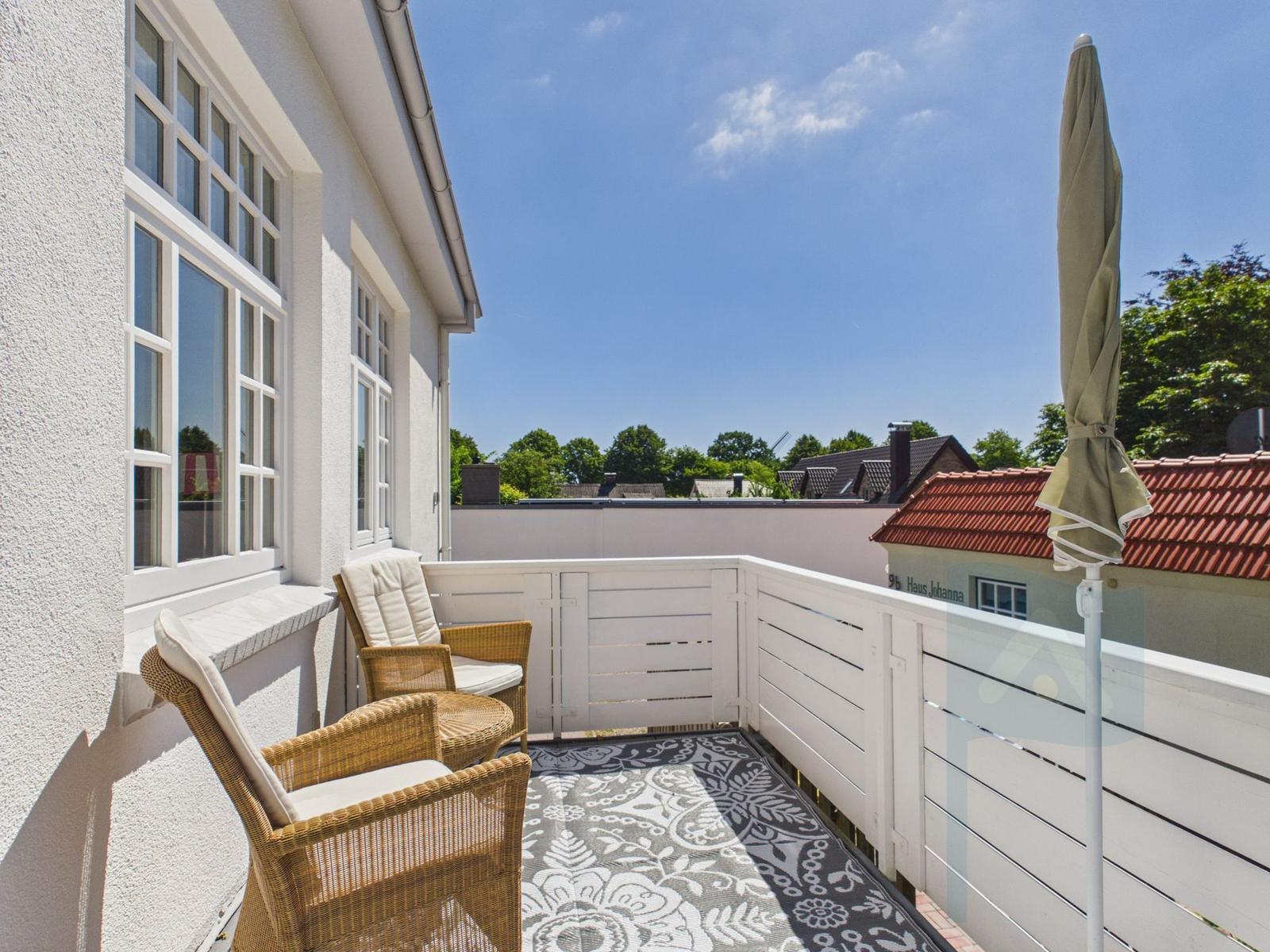 Terrasse mit zwei Stühlen, Sonnenschirm und Teppich. Blick auf Dächer und Bäume.