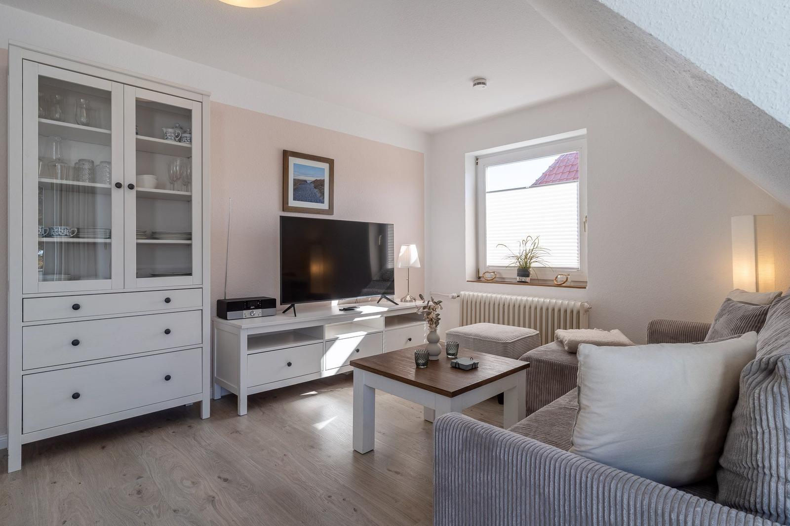 Wohnzimmer mit Sofa, Fernseher und Glasvitrine. Fenster mit Blick auf Dach.