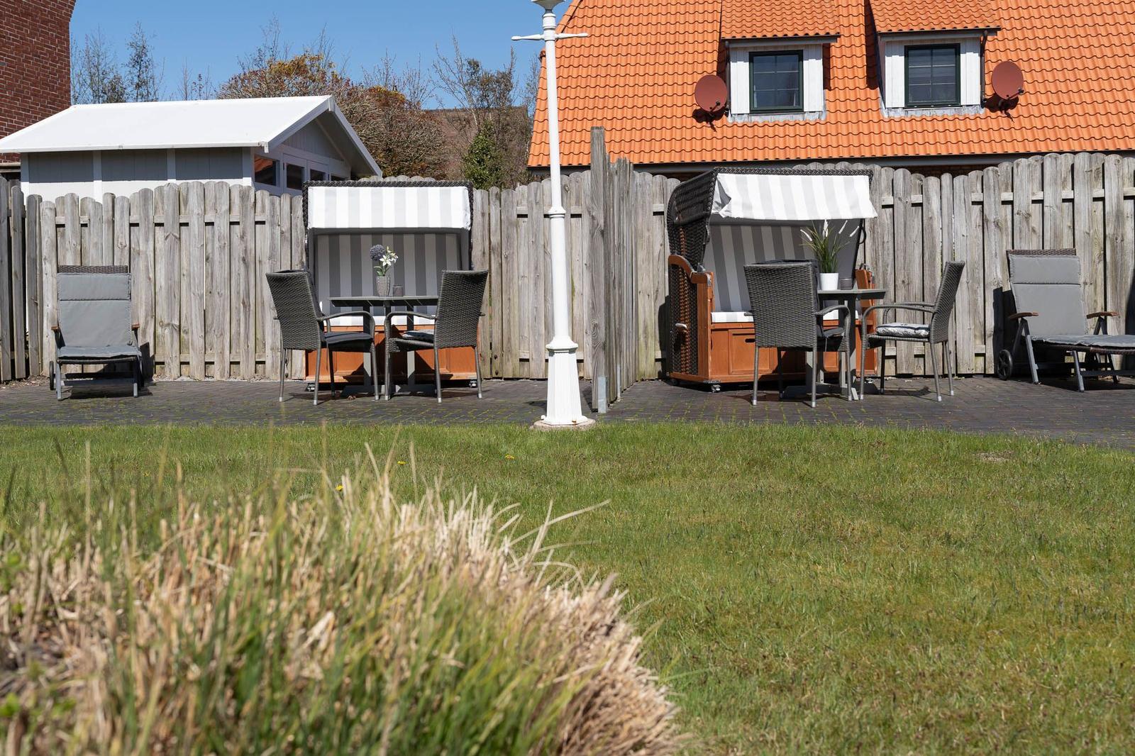 Hinterhof mit Terrasse, Garten und Gartenmöbeln vor einem Haus mit rotem Dach.