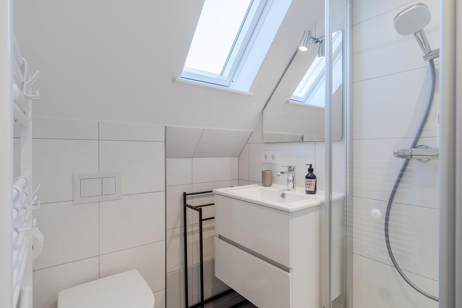 Badezimmer mit Dusche, Waschbecken und Toilette unter Dachschrägen mit Dachfenster.