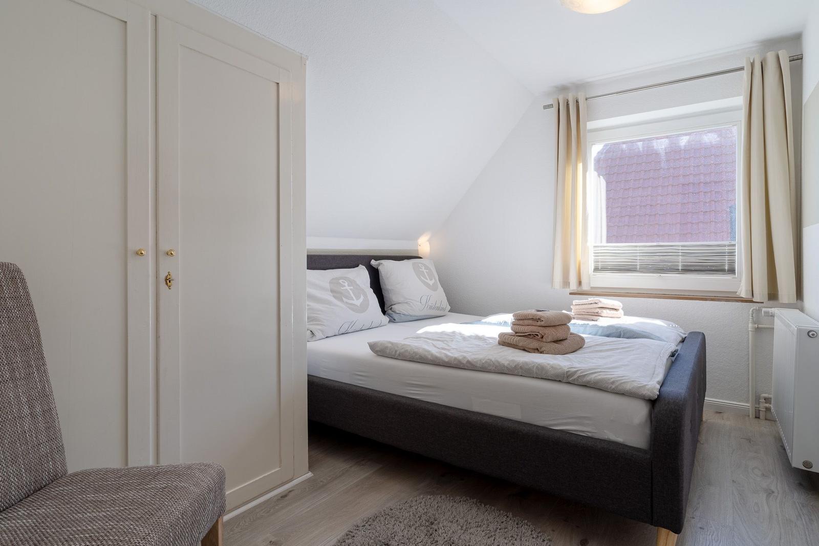 Schlafzimmer mit Doppelbett, Kleiderschrank und Fenster mit Vorhängen.