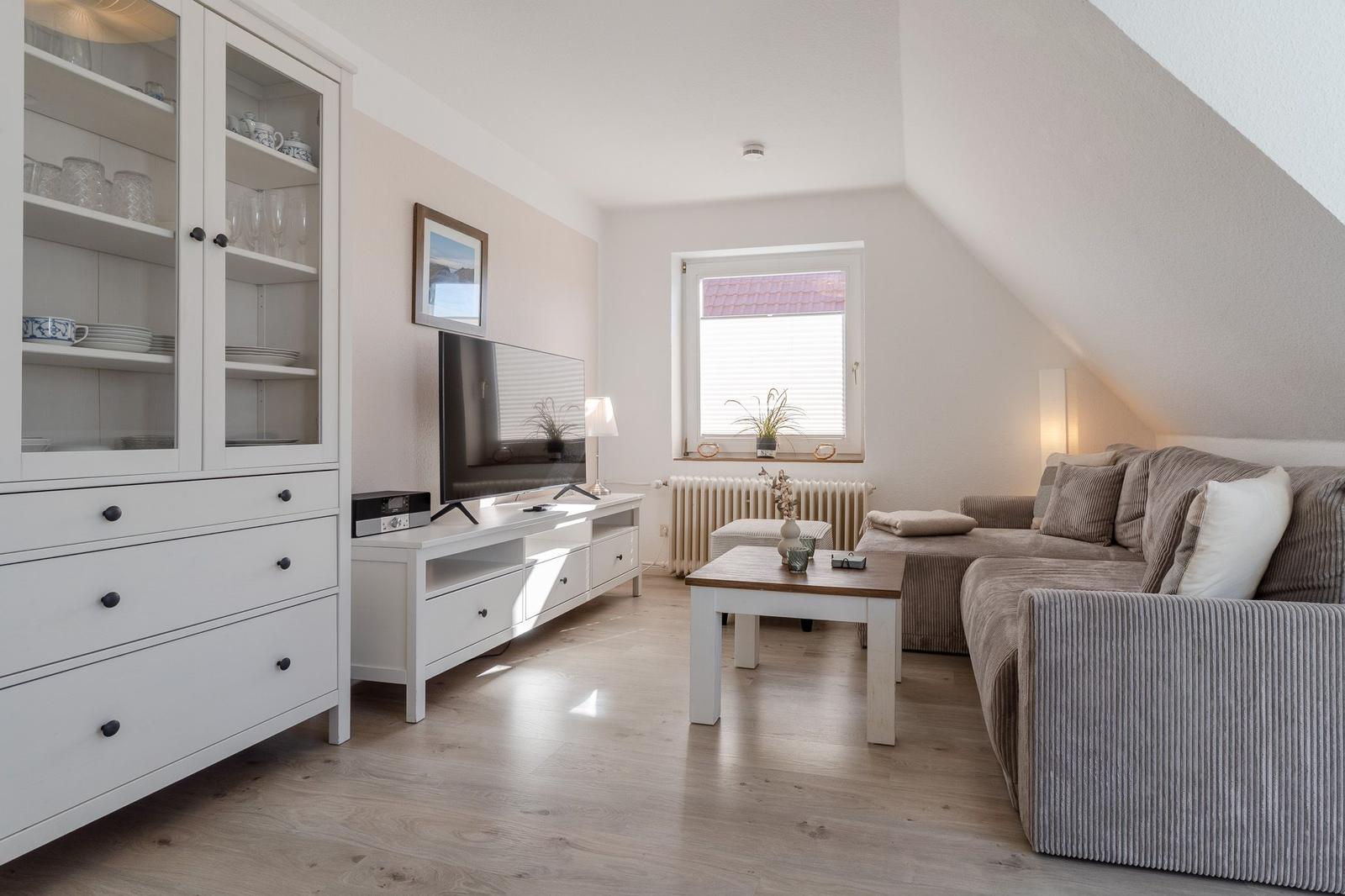 Wohnzimmer mit Sofa, Fernseher und Glasvitrine. Holzboden und Dachschräge.