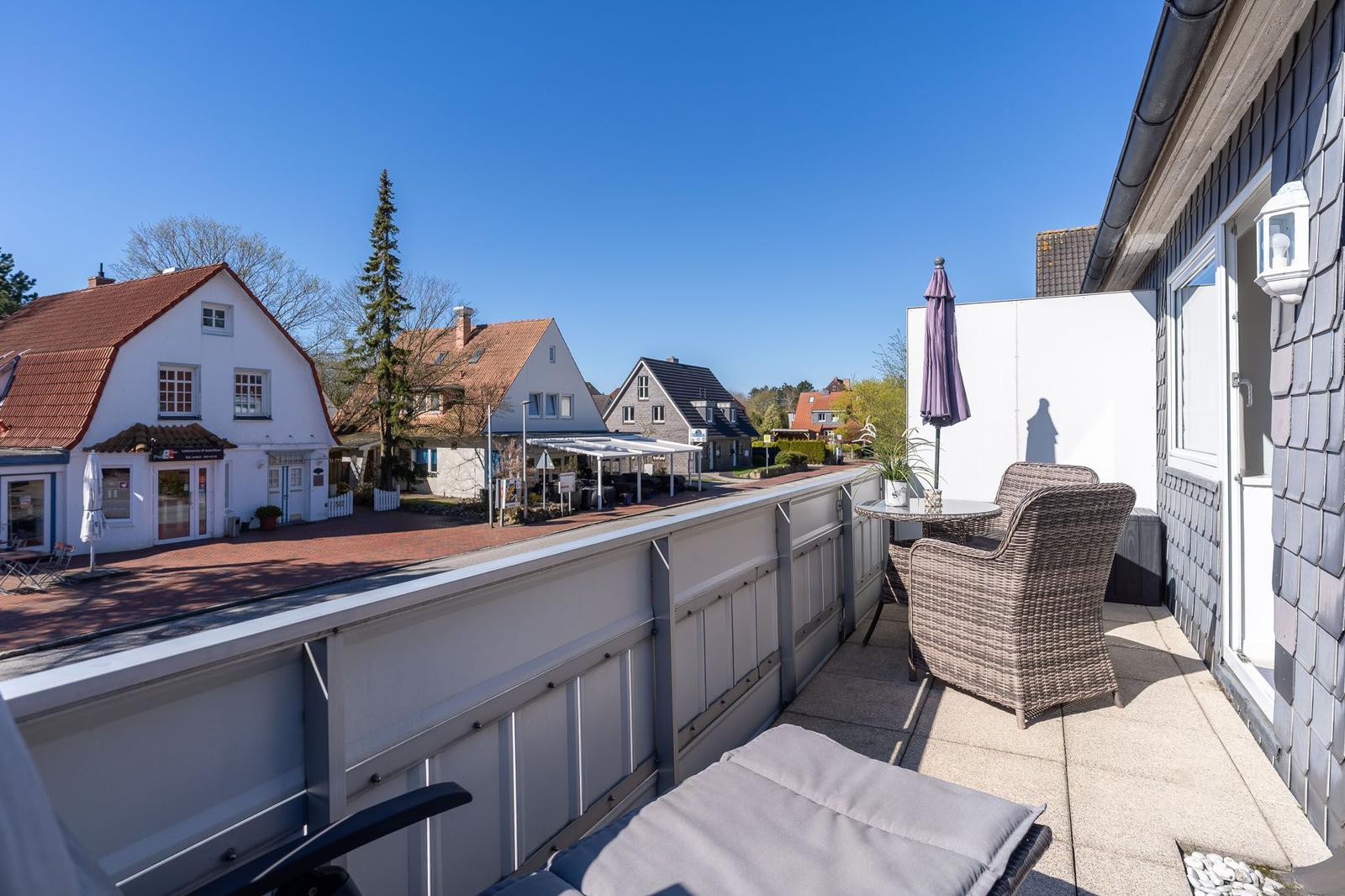 Terrasse mit Liegestuhl, Tisch und Stühlen. Blick auf Straße und Häuser im Hintergrund.