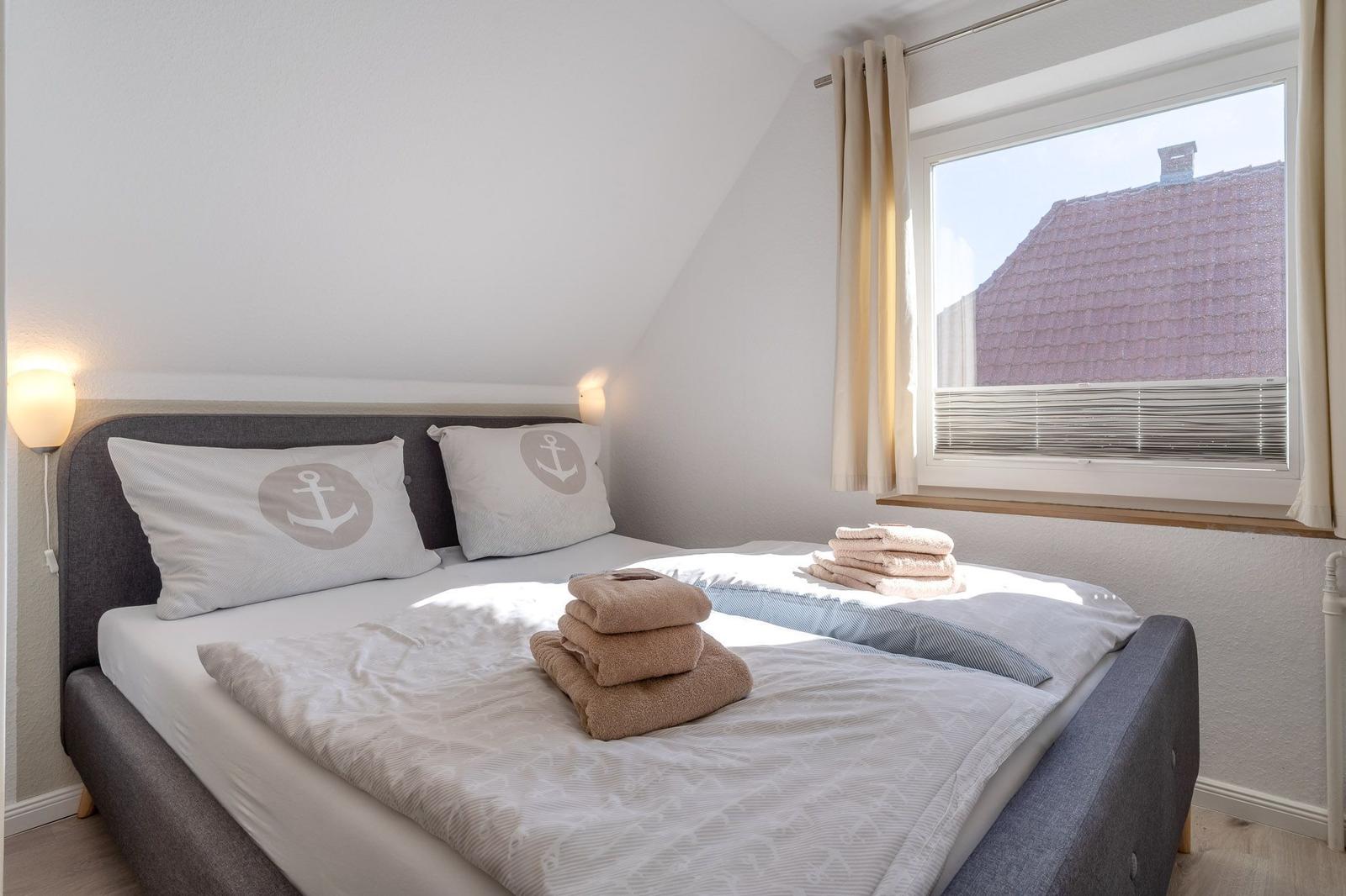 Doppelbett mit Kissen und Handtüchern. Fenster mit Jalousie und Vorhang.