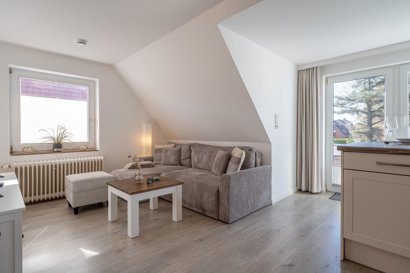 Wohnbereich mit Schlafsofa, Tisch und Fenster. Holzboden und Schiebetür zur Terrasse.