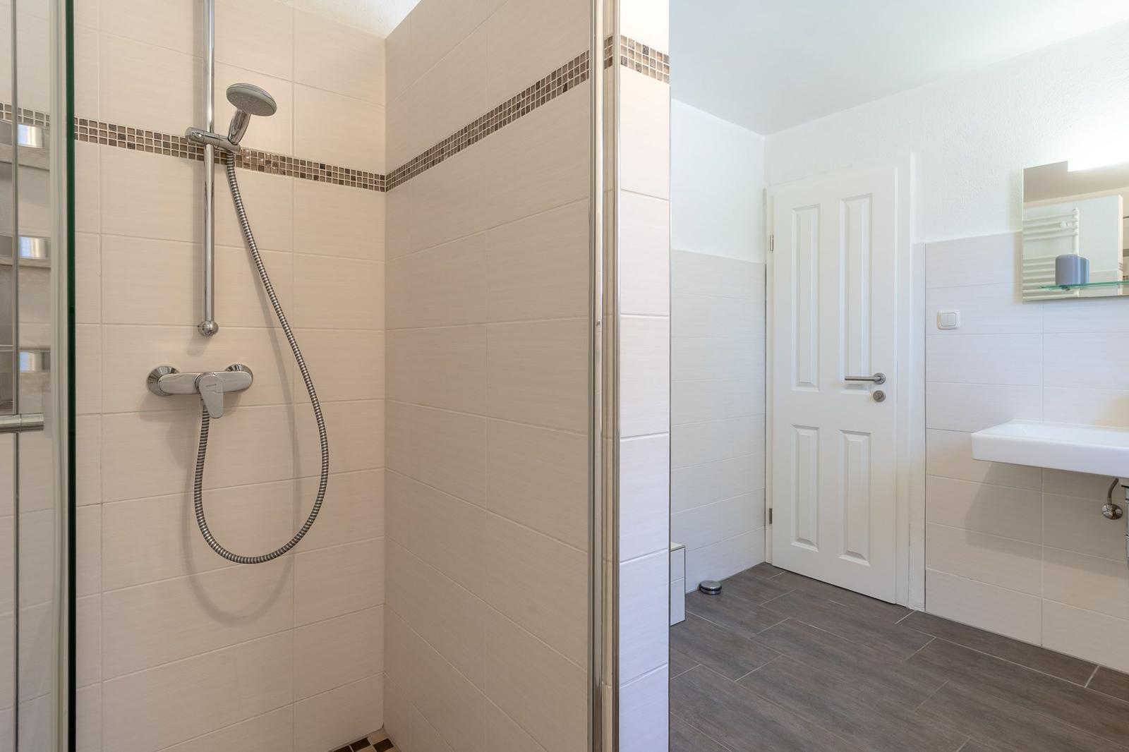 Dusche mit Duschbrause, Waschbecken und Spiegel
