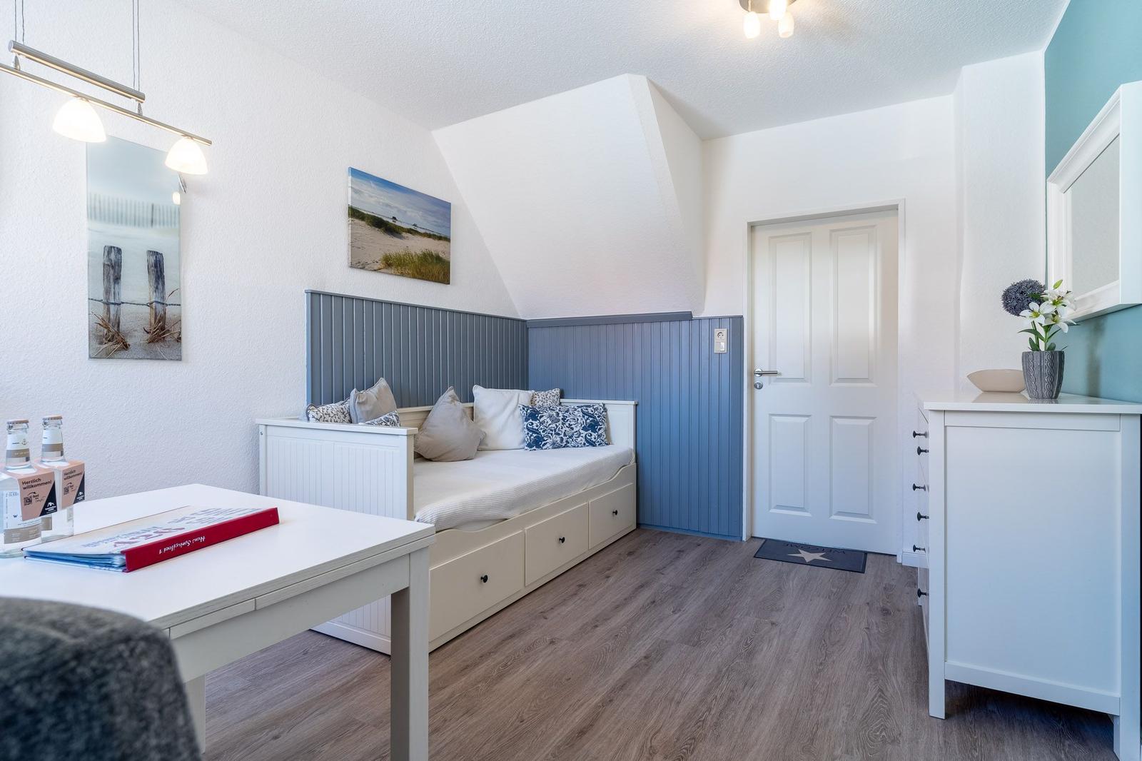 Schlafzimmer mit Bett, Tisch und Schrank. Wandgestaltung in Blau und Weiß.