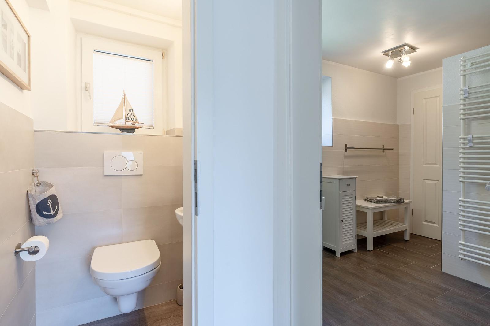Badezimmer mit Toilette, Fenster und nautischem Dekor. Nebenraum mit Waschtisch und Heizkörper.