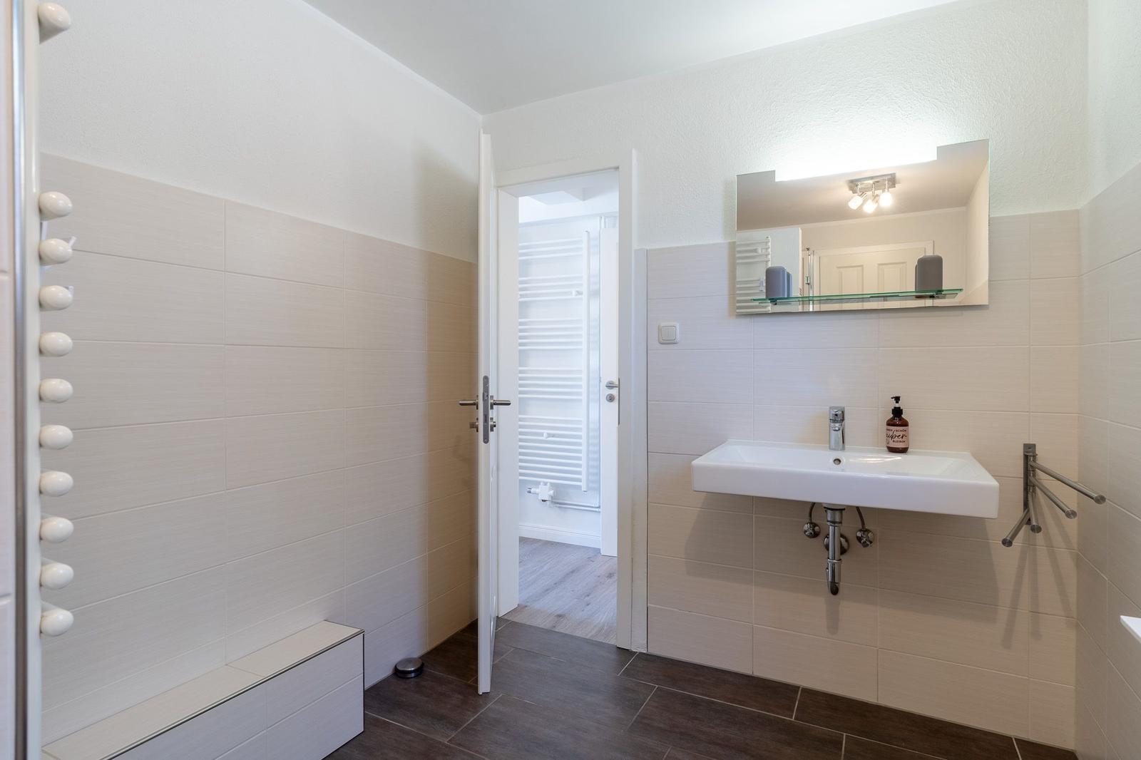Badezimmer mit Waschbecken, Spiegel und Tür zum Duschbereich.