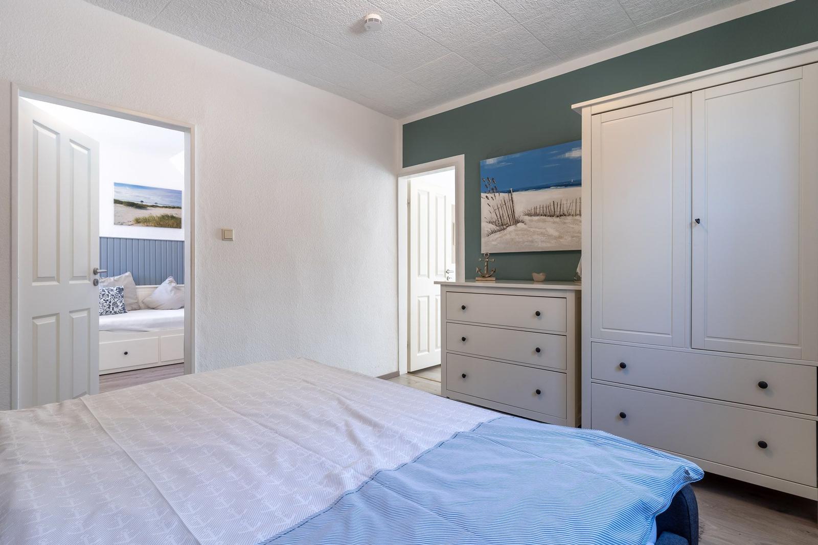 Schlafzimmer mit Bett, Kleiderschrank und Schminktisch. Tür führt zu einem weiteren Raum.
