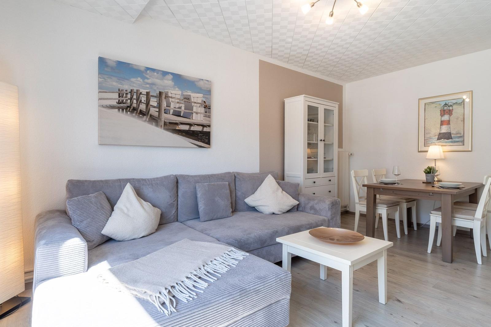 Wohn- und Essbereich mit Sofa, Tisch und Wandbildern.