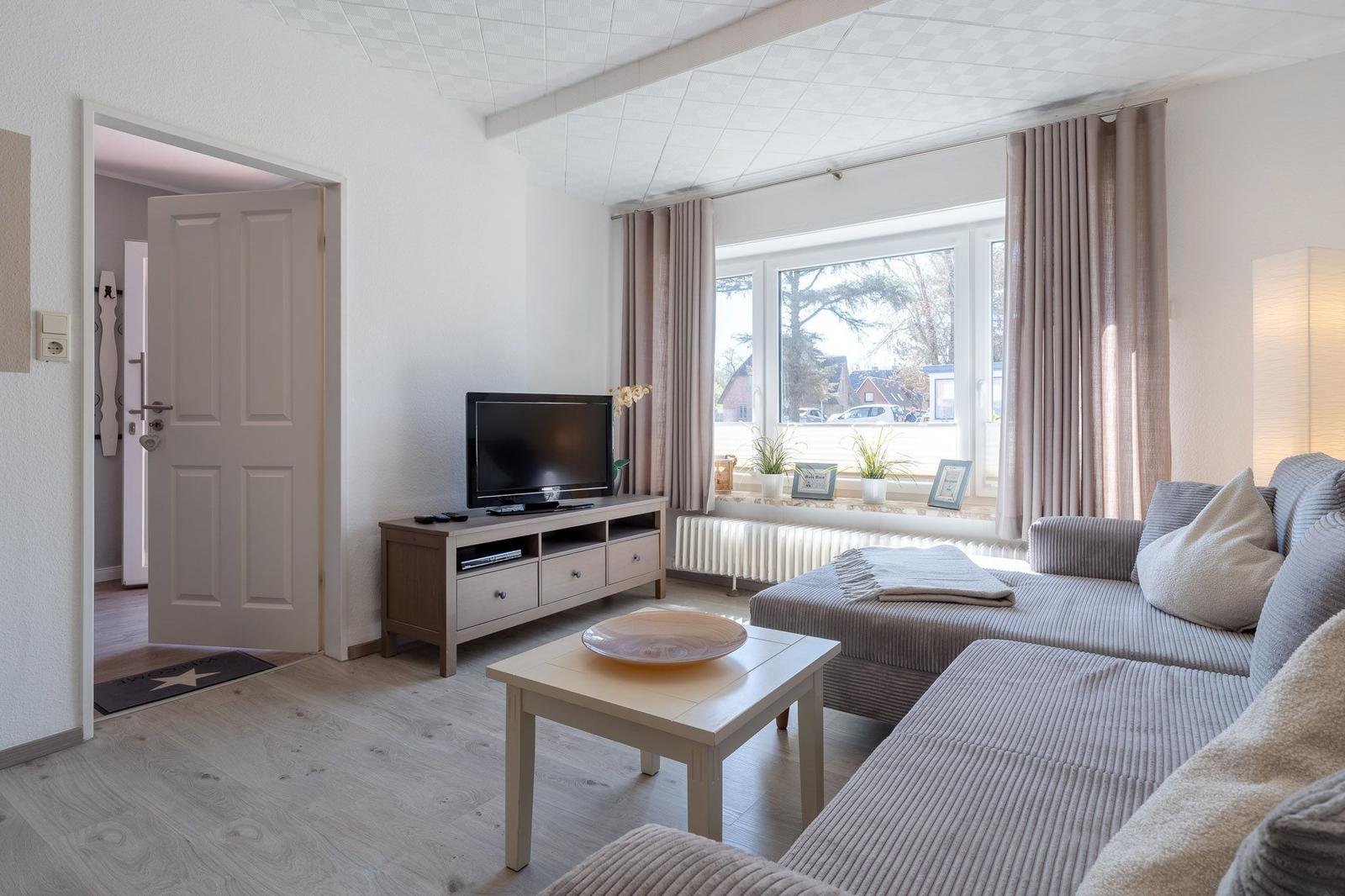 Wohnzimmer mit Sofa, Fernseher und Fenster. Tür führt in den Flur.