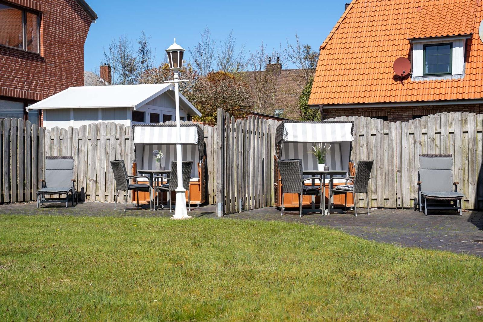 Hinterhof mit Grillplatz, Sitzgelegenheiten und Holzzaun. Grasfläche und Terrassenbereich.