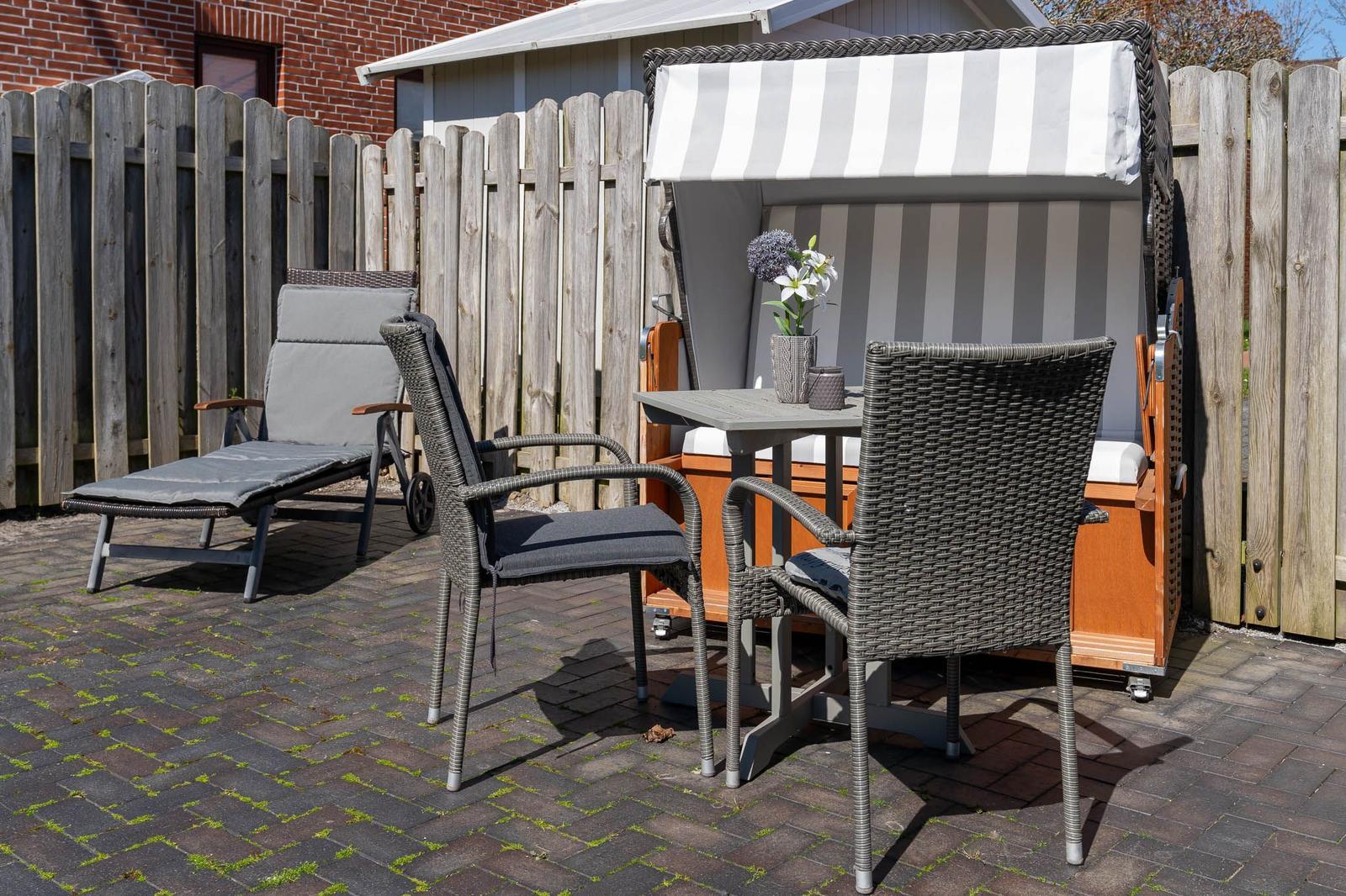Terrasse mit Liegestuhl, zwei Stühlen und Tisch neben Strandkorb.