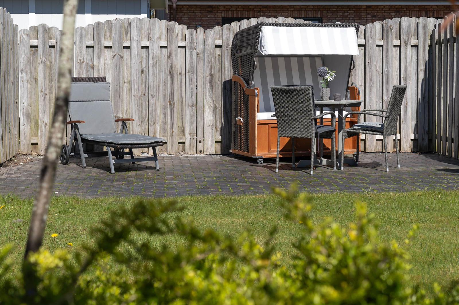 Garten mit Liegestuhl, Hängesessel und Tisch mit Stühlen auf gepflastertem Boden.
