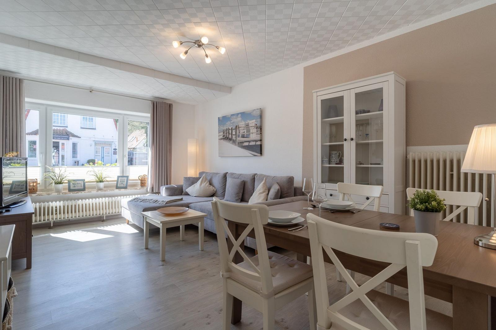 Wohn- und Essbereich mit Sofa, Tisch und Stühlen. Fenster mit Blick auf Straße.