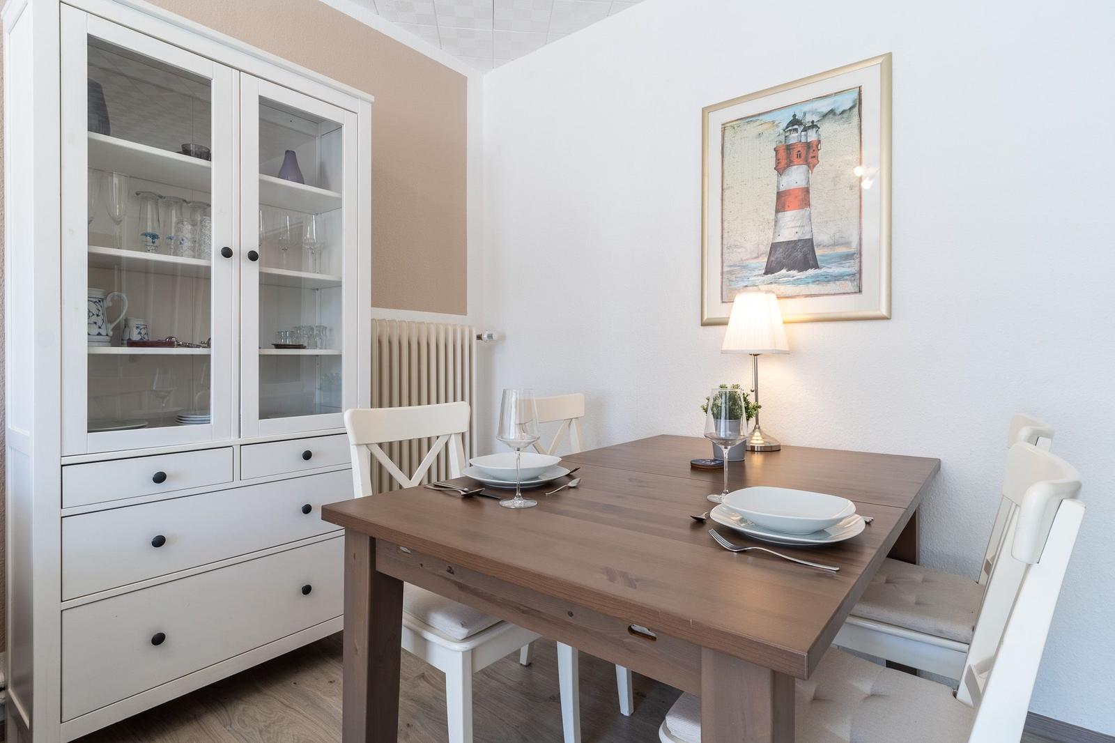 Esstisch mit Stühlen, Sideboard und Leuchte an der Wand.