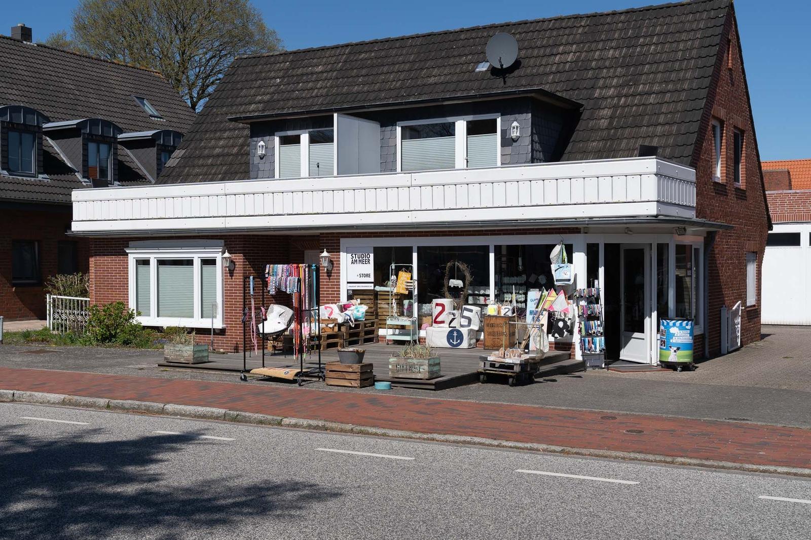 Ein Haus mit Laden im Erdgeschoss und Balkon im Obergeschoss. Vor dem Laden sind verschiedene Artikel ausgelegt.