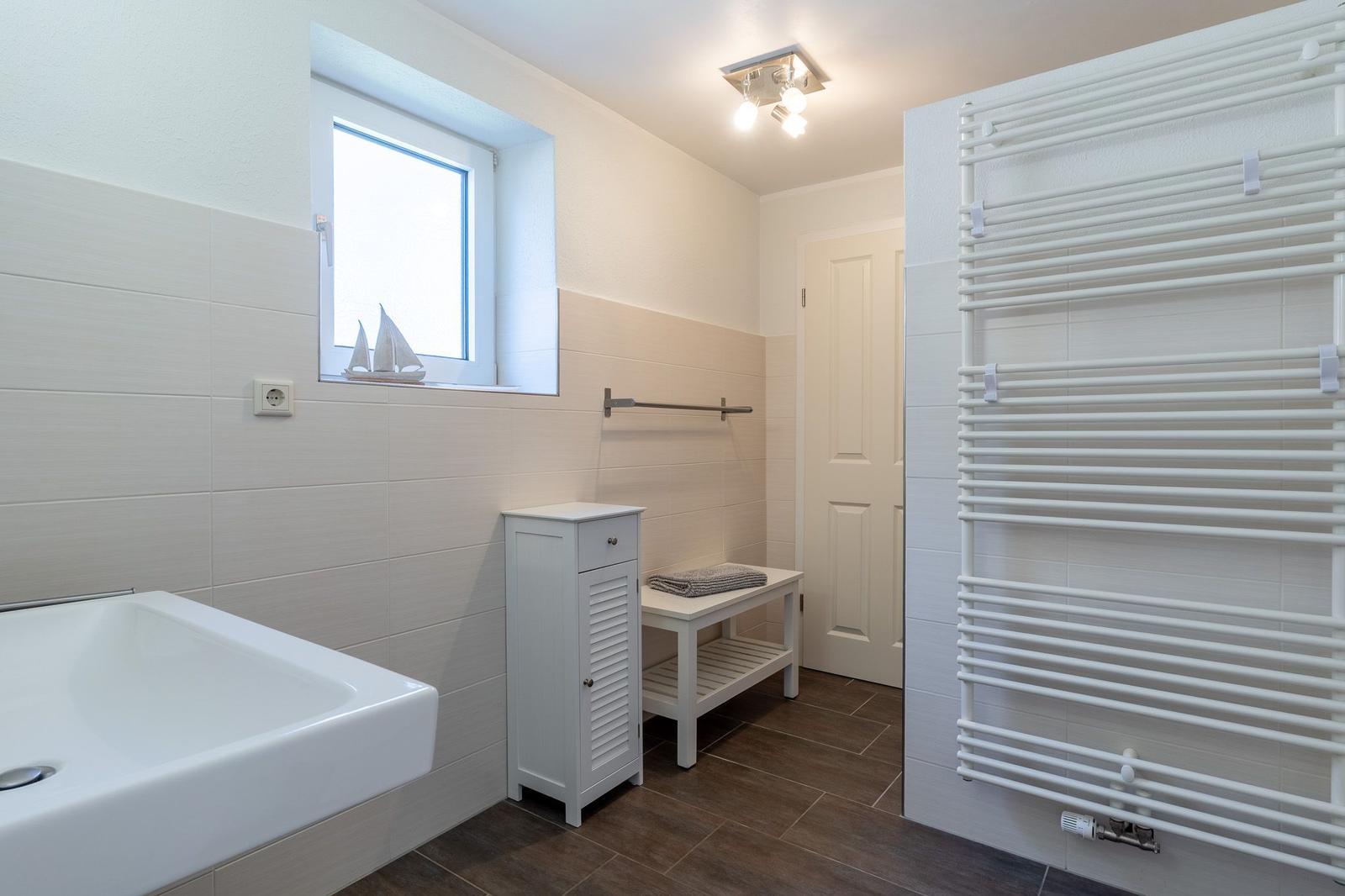 Badezimmer mit Badewanne, Heizkörper und Fenster mit Segelbootmodell.