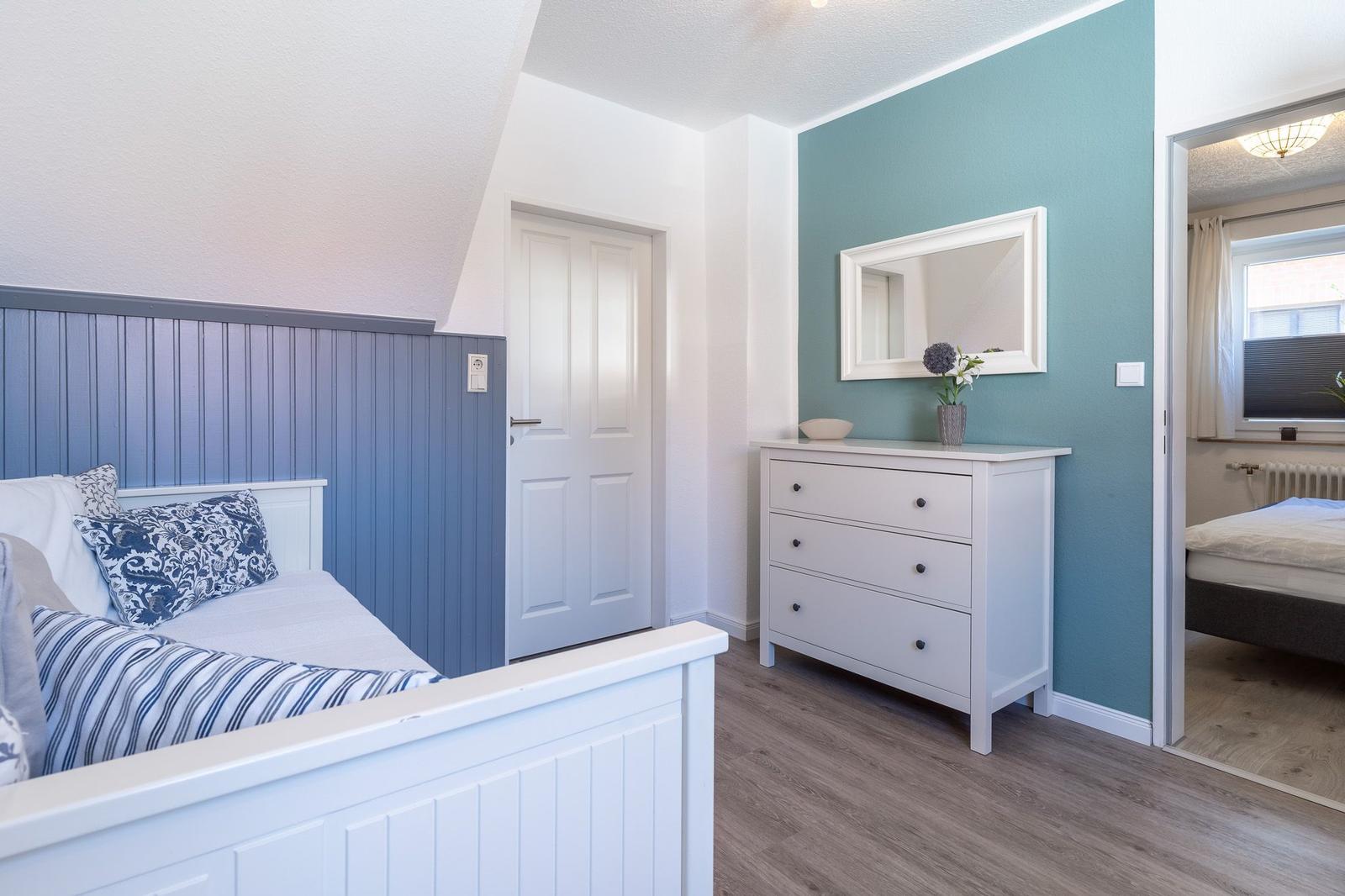 Schlafzimmer mit Bett, Schrank und Spiegel an türkisfarbener Wand.