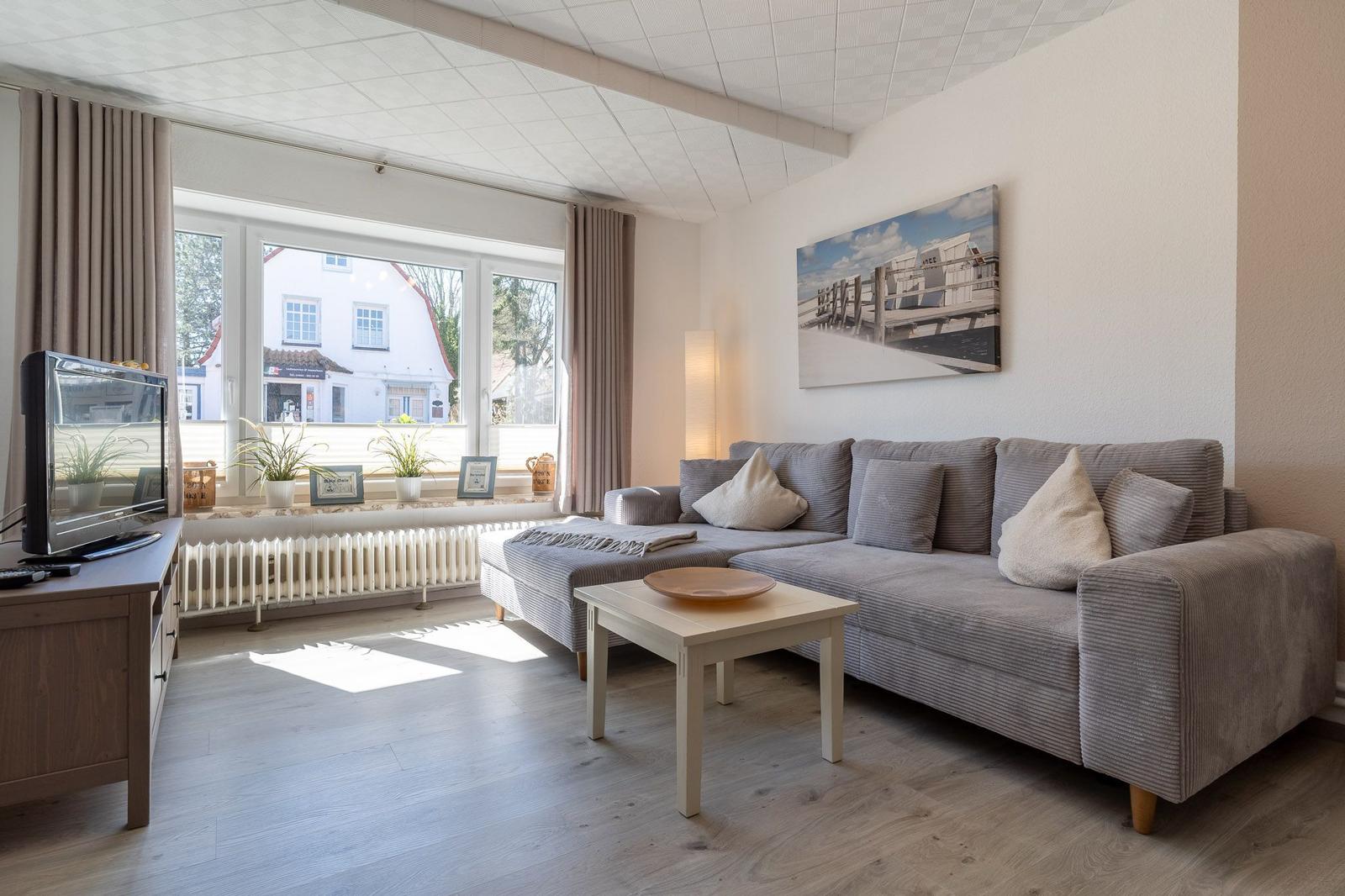 Wohnzimmer mit Sofa, Couchtisch und Fernseher. Fenster mit Blick auf Straße.