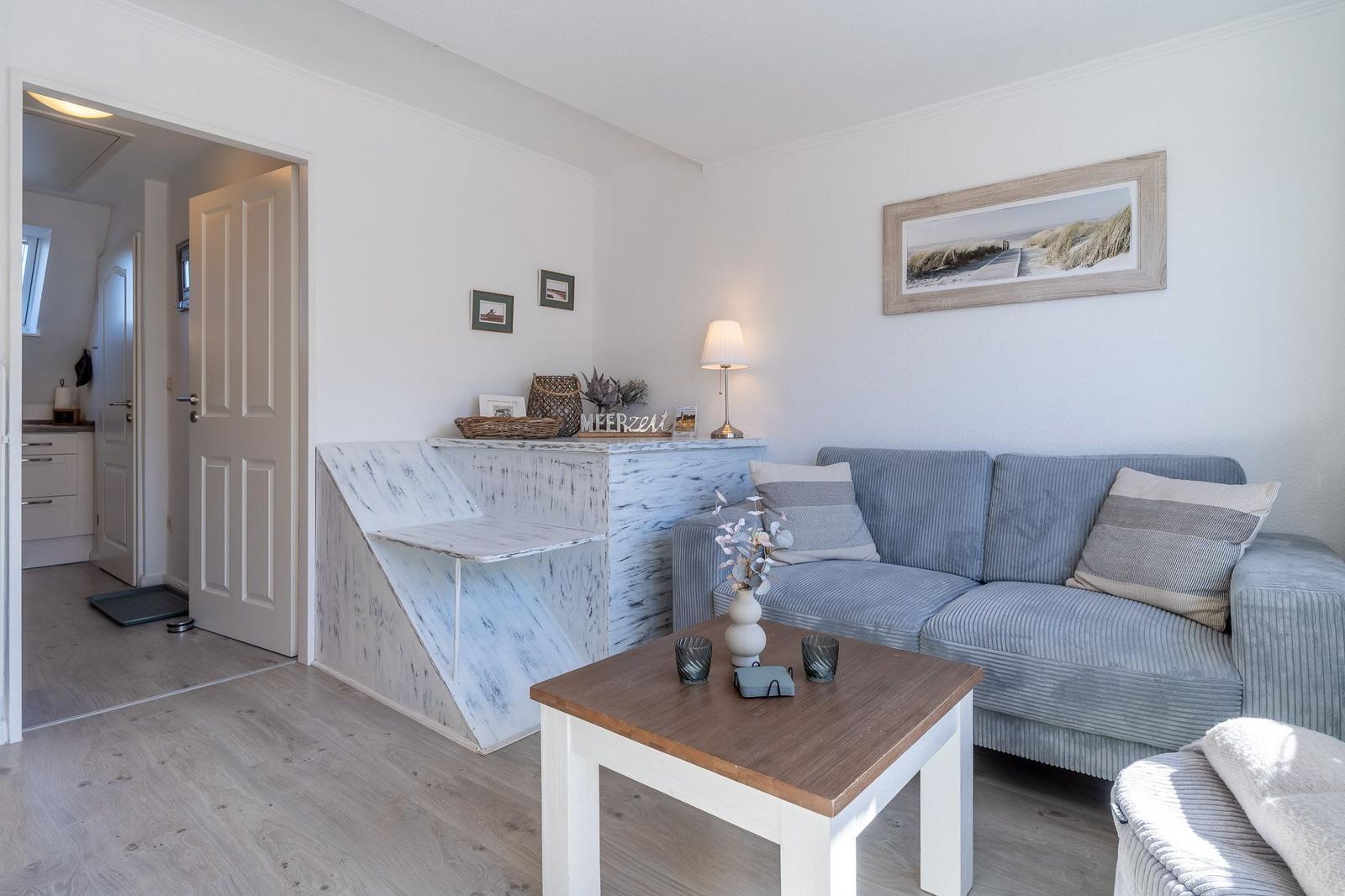 Wohnzimmer mit Sofa, Couchtisch und Wandbild. Durchgang zur Küche sichtbar.