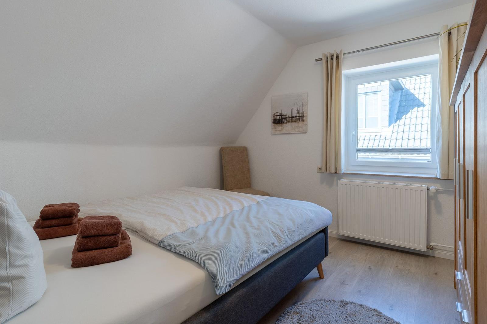 Schlafzimmer mit Dachschräge, Bett, Fenster und Kleiderschrank.