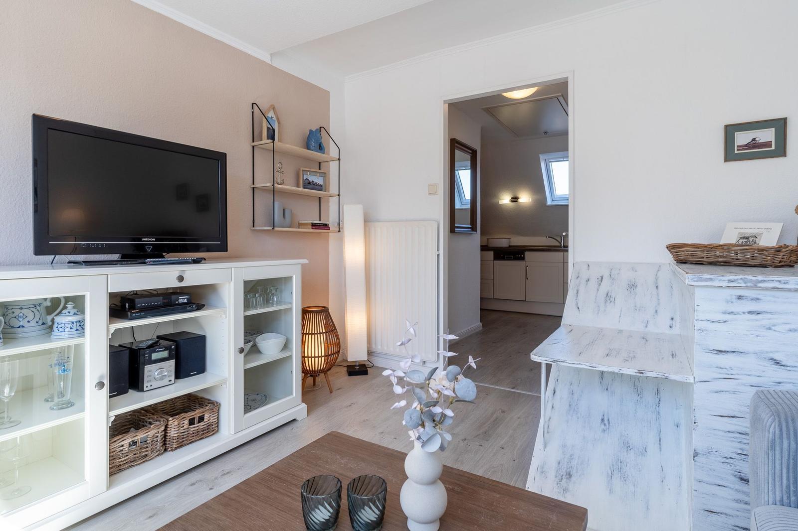 Wohnzimmer mit TV, Sideboard und Blick in die Küche.