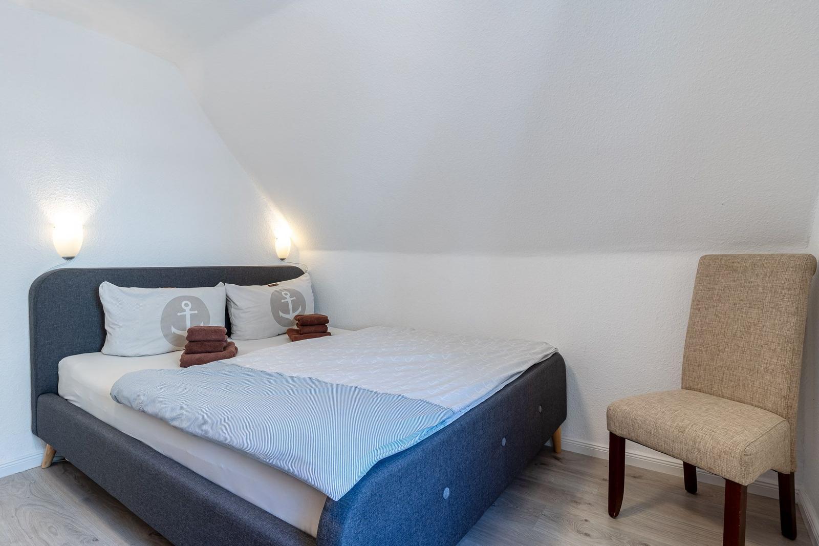 Schlafzimmer mit Bett, Stuhl und Stehlampe an der Wand.