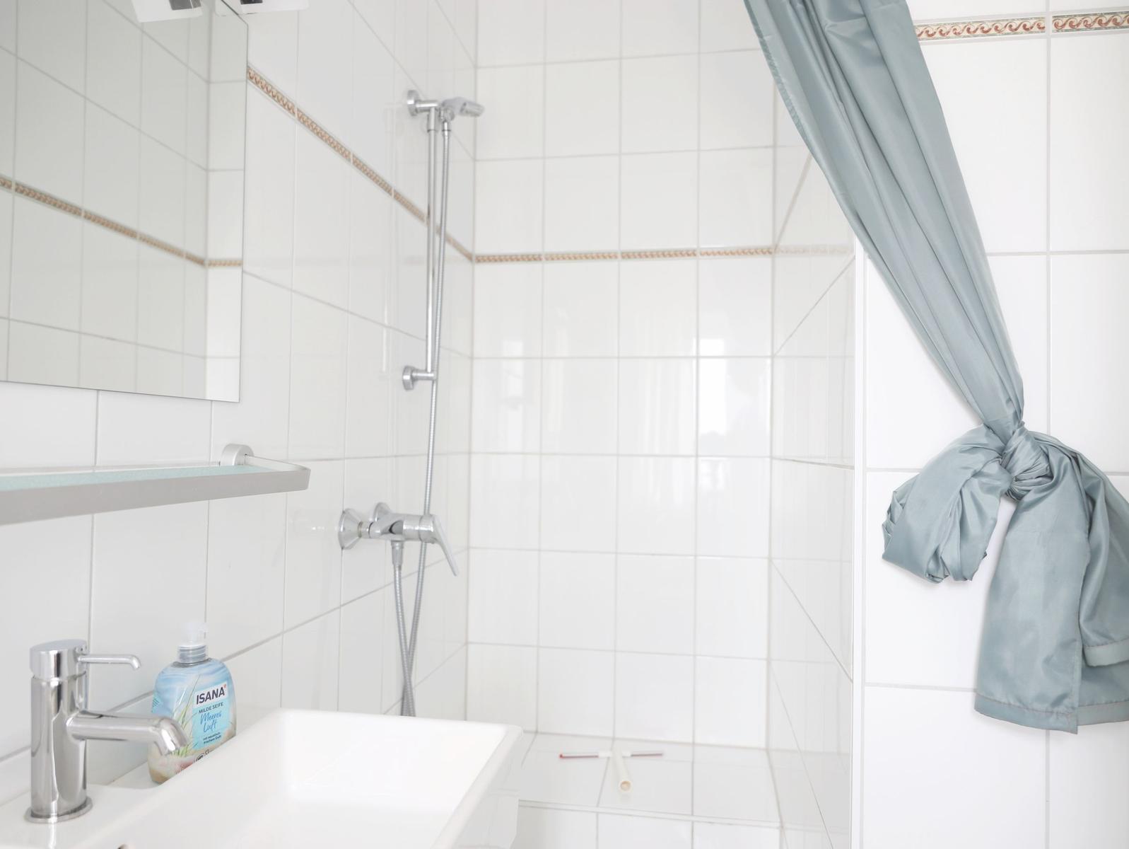 Badezimmer mit Dusche, Waschbecken und grauem Duschvorhang.