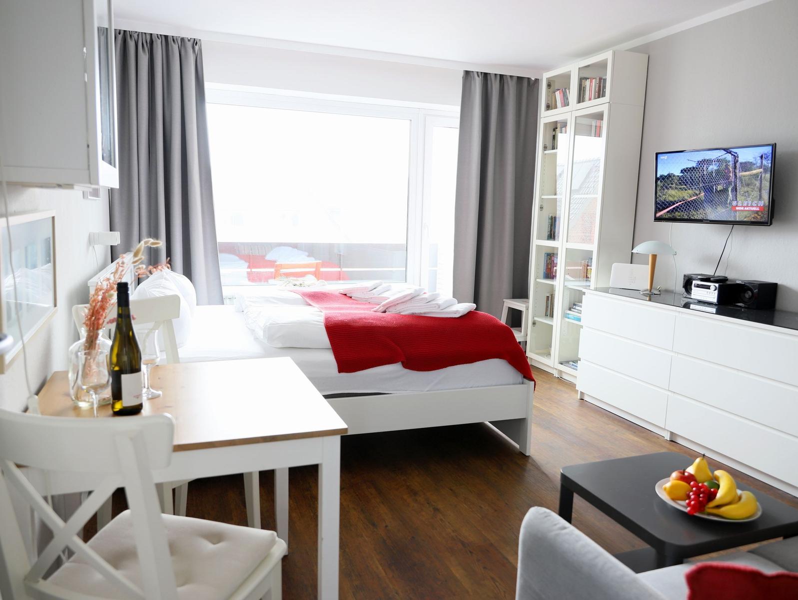 Schlafzimmer mit Bett, TV, Bücherregal und Tisch mit Stühlen.