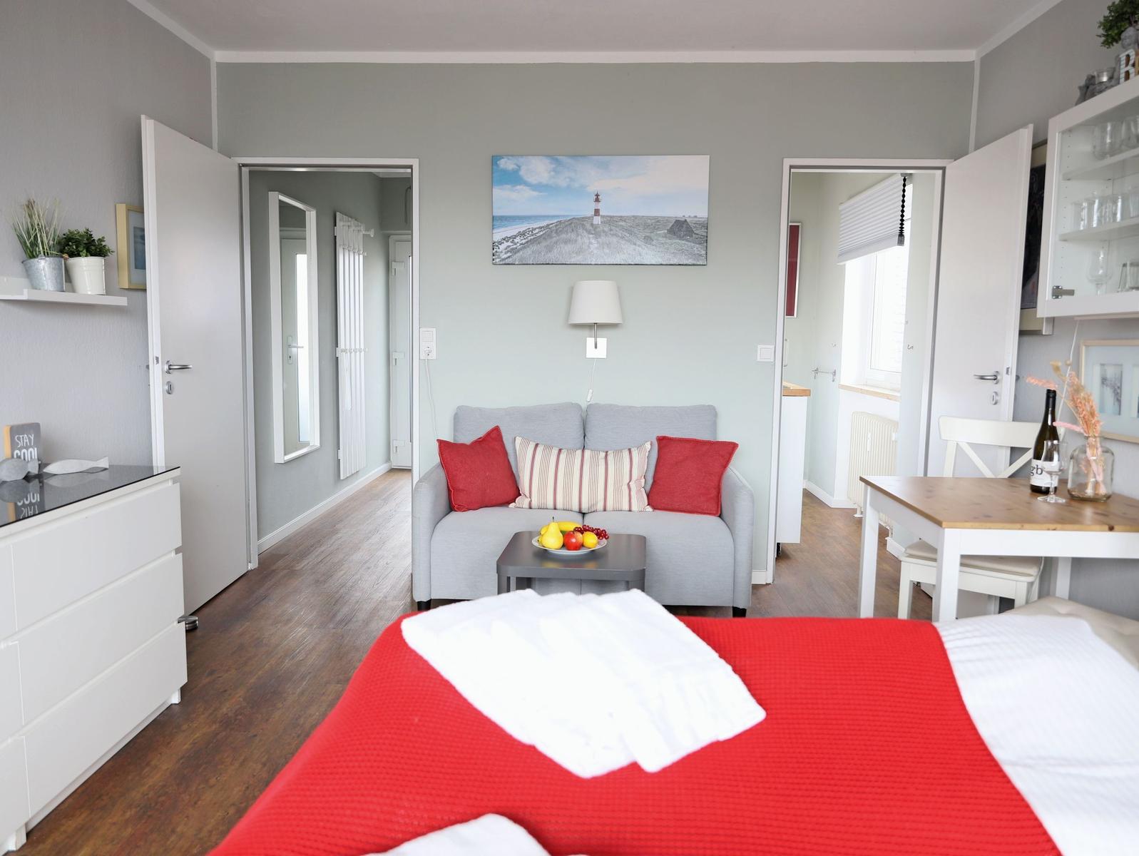 Ein Schlafzimmer mit rotem Bett, grauem Sofa und Wandbild mit Leuchtturm.