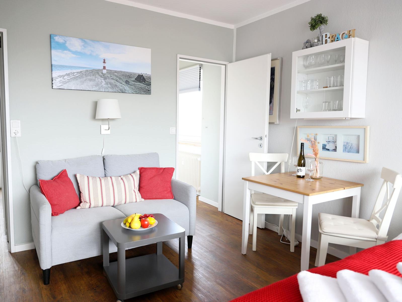 Wohnbereich mit Sofa, Esstisch und Küchenzeile. Wandbild zeigt Leuchtturm.
