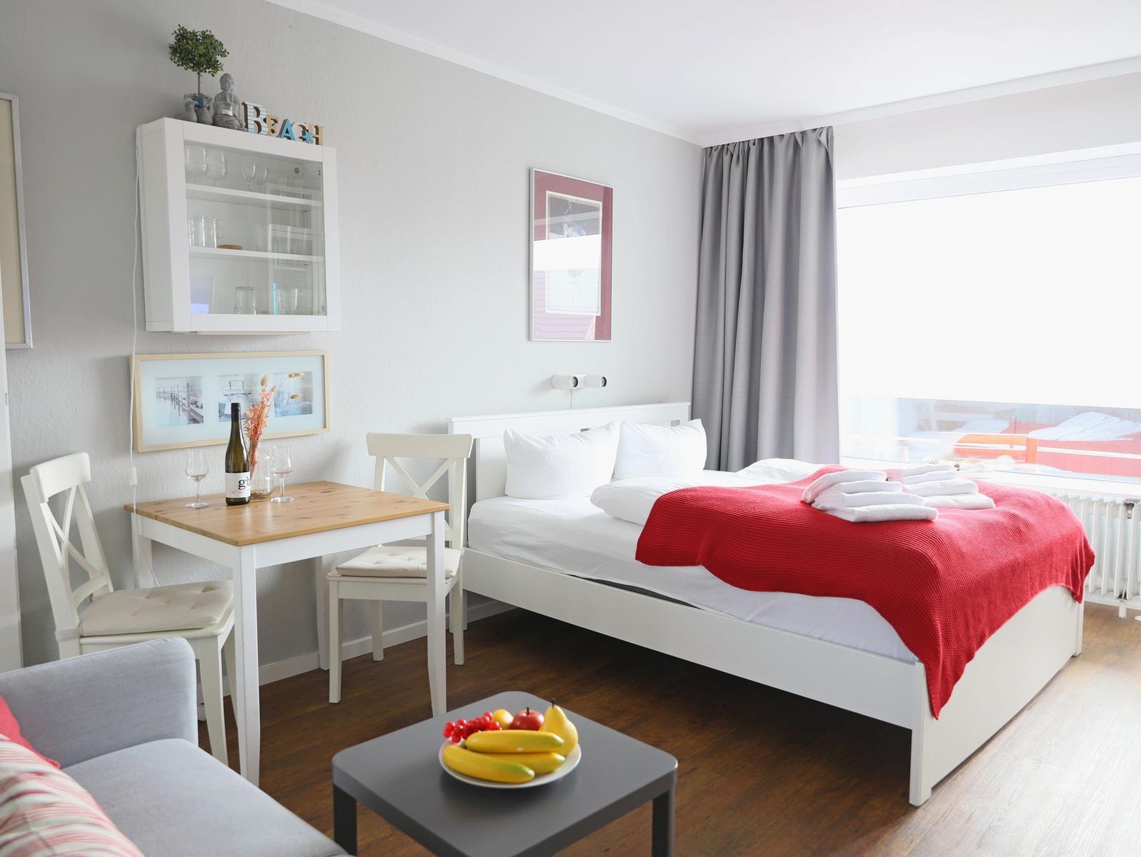 Schlafzimmer mit Bett, Tisch, Stühlen und Fenster. Auf dem Tisch steht eine Flasche Wein.