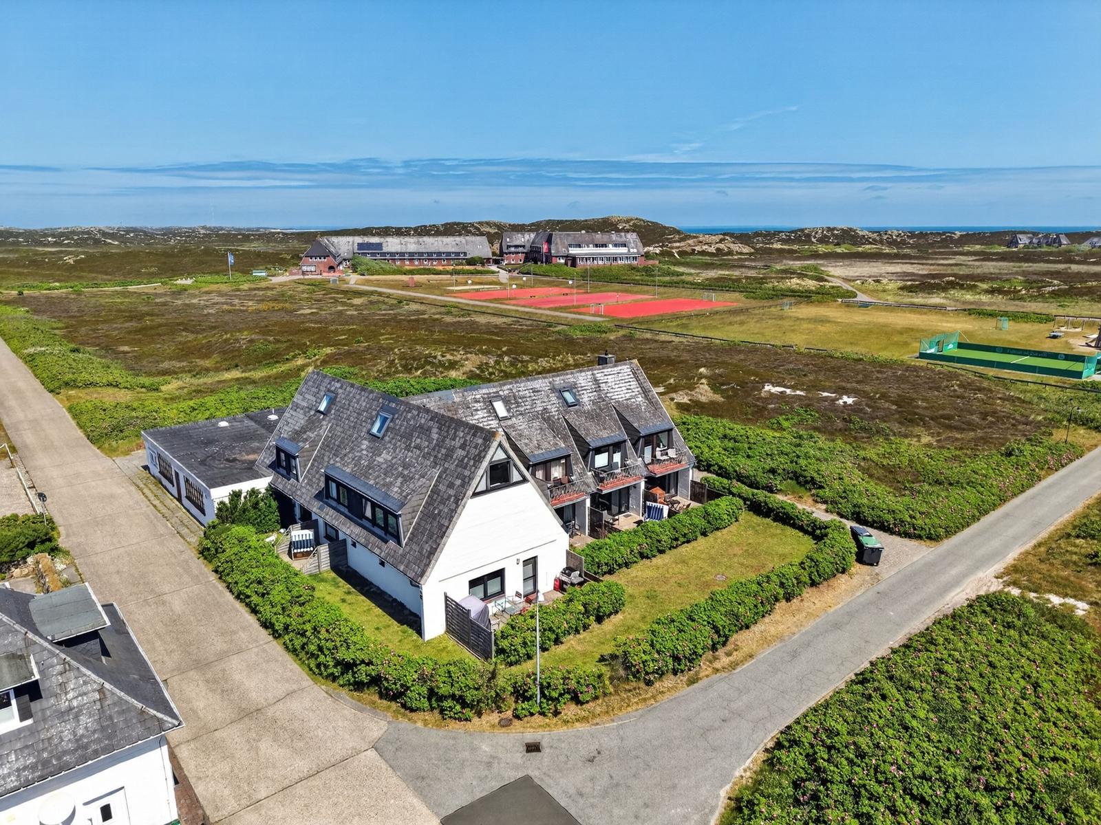 Wohnhaus mit Terrasse, umgeben von Grünflächen und Tennisplätzen. Blick aufs Meer.