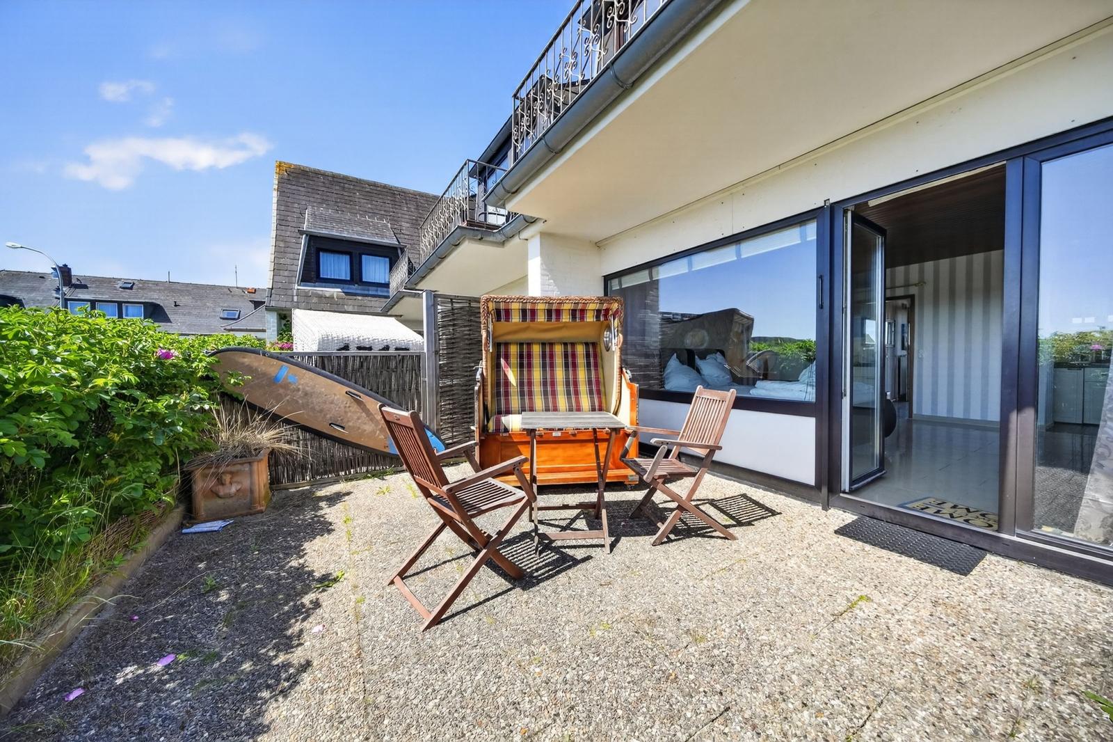 Terrasse mit Liegestuhl, Tisch und Stühlen. Durchgehende Glastüren führen ins Haus.