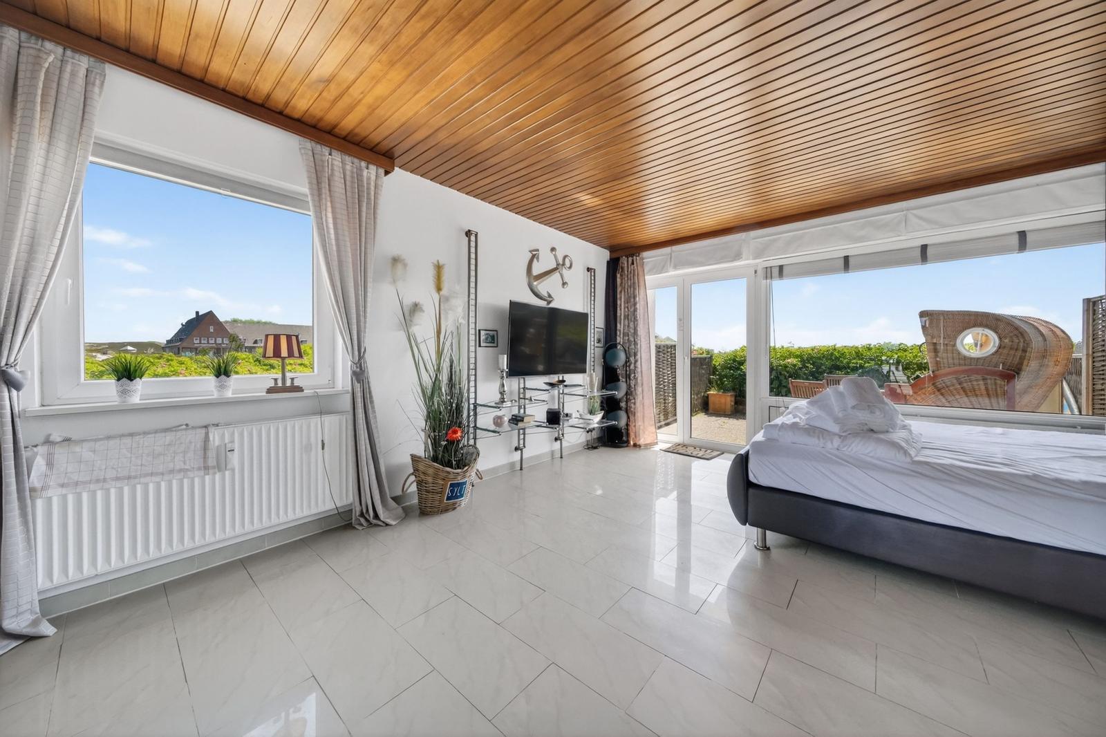 Schlafzimmer mit Blick auf Garten und Landschaft. Holzdecke, großes Bett und TV.