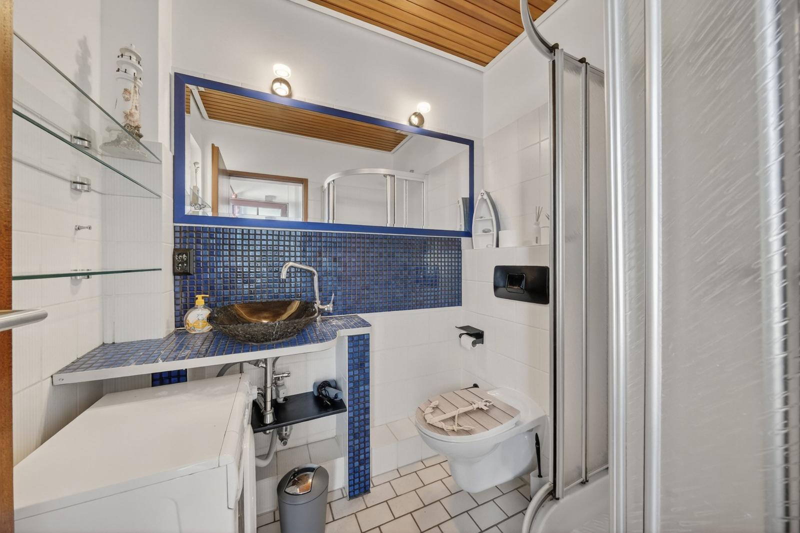 Badezimmer mit blauen Fliesen, Waschbecken, Toilette und Dusche.