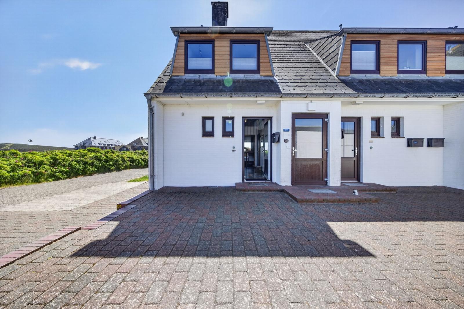 Modernes Haus mit weißer Fassade, Holzverkleidung und Dachfenstern. Vordere Terrasse mit Pflastersteinen.