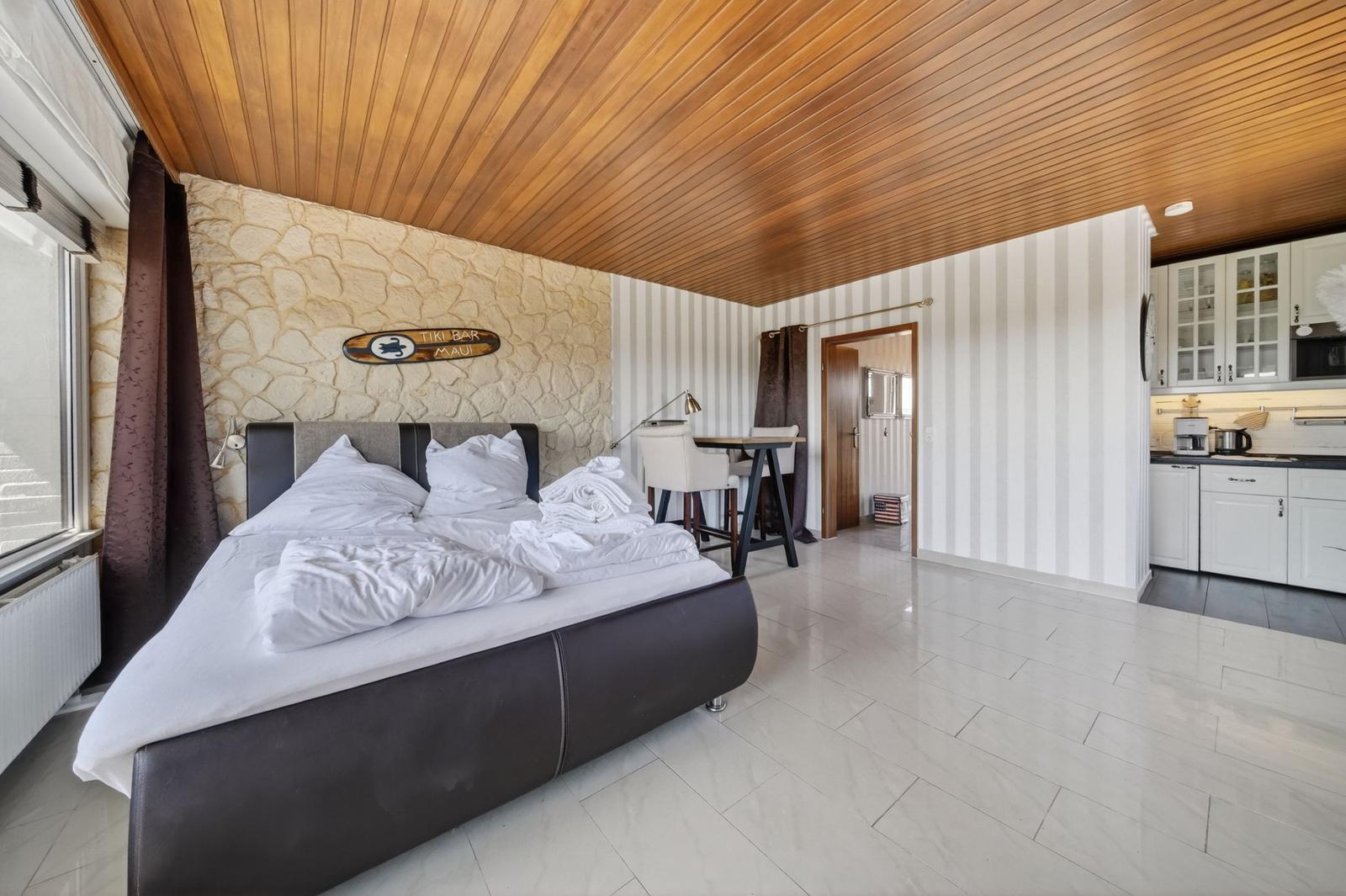 Schlafzimmer mit Bett, Küchenbereich und Holzdecke. Steinwand und Streifenwand.