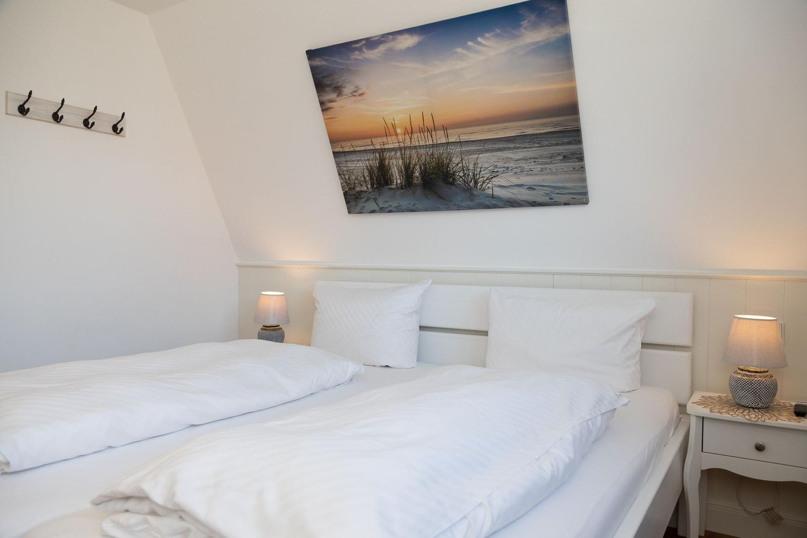 Schlafzimmer mit Doppelbett, Wandbild und Nachttischen mit Lampen.