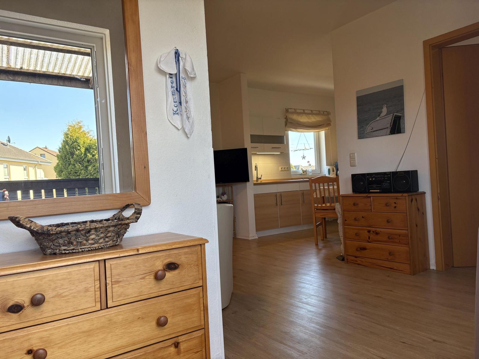 Wohnraum mit Holzmöbeln, Küchenbereich und Fensterblick auf Balkon.