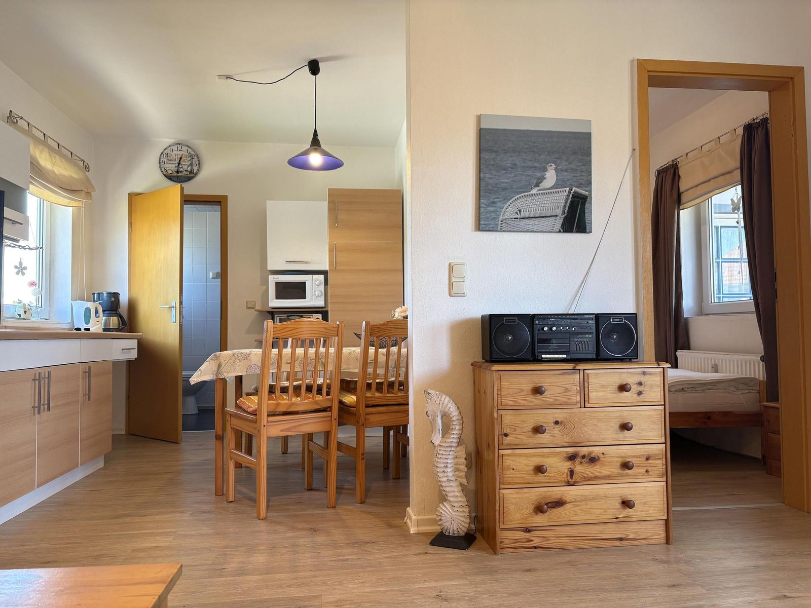 Wohnung mit Essbereich, Schlafzimmer und Küchenzeile. Holzmöbel und Wandbild mit Seemöwe.